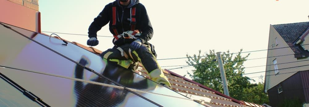 Person auf Dach installiert Solarmodule. Das Logo der Marke otovo ist abgebildet